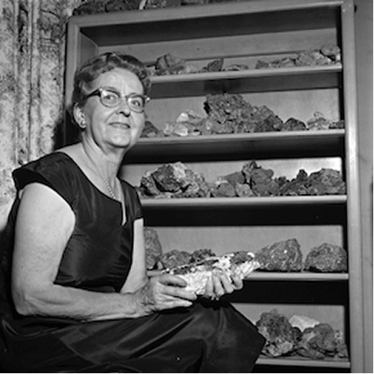 Black and white photo of a woman sitting in front of a bookcase full of rocks